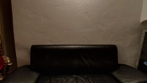 A black leather sofa against a textured wall with a wall-mounted light fixture above it. - Apartment for couples and artisans (Ehingen (Donau))