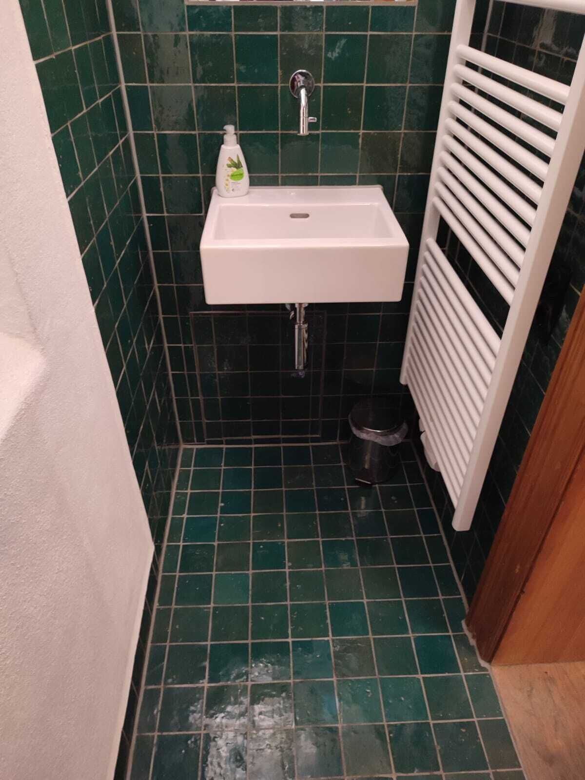 A small bathroom with a white sink, green tiled walls, and a white radiator.