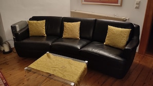 A black leather sofa with yellow cushions, a small table with a yellow tablecloth, and a framed artwork on the wall. - Apartment for couples and artisans (Ehingen (Donau))