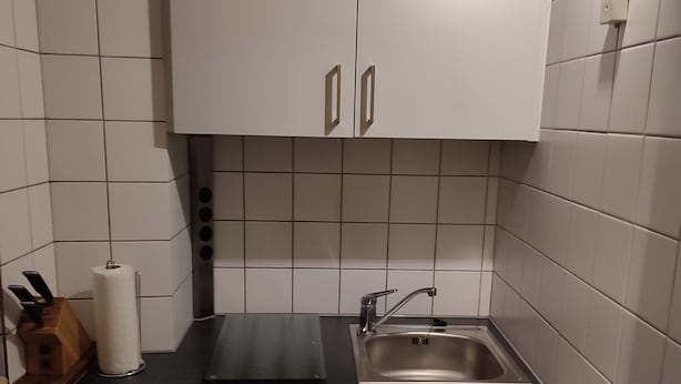 A small kitchen with white cabinets, a black countertop, and a stainless steel sink. - Apartment for couples and artisans (Ehingen (Donau))