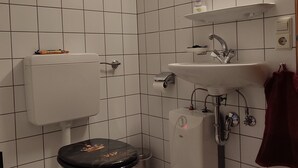 A bathroom with white tiled walls, a toilet, a sink, and a mirror. - Apartment for couples and artisans (Ehingen (Donau))