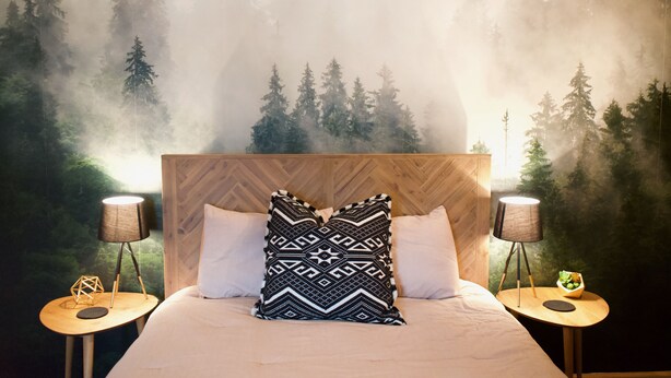 Ein Schlafzimmer mit einem Bett, zwei Nachttischen und einem Wandbild von einem Wald.
