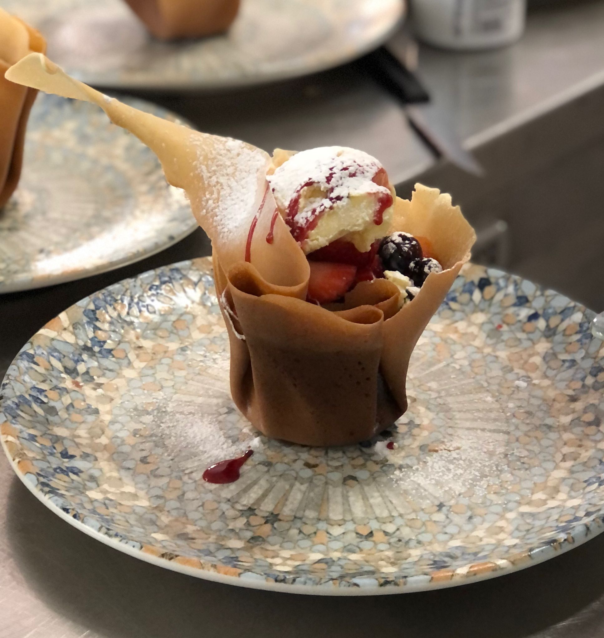 A dessert in a paper cup on a mosaic-patterned plate.