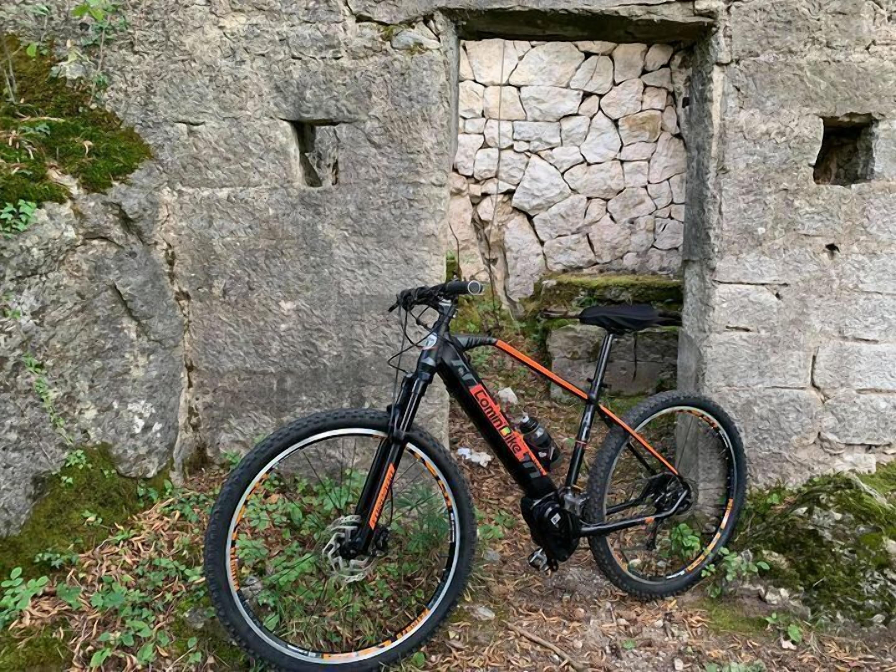 Una bicicleta de montaña apoyada contra un muro de piedra con un ventanal pequeño.
