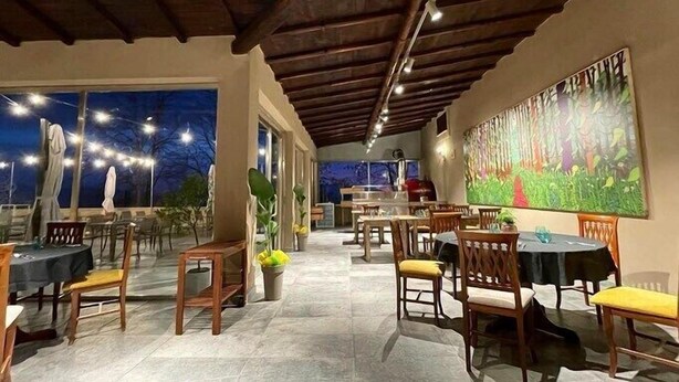 An indoor dining area with wooden tables and chairs, a large painting on the wall, and a view of the night sky through large windows. - Villa Grancassa (San Donato Val Di Comino)