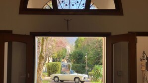 A view through an open door into a driveway with a classic car parked in front. - Villa Grancassa (San Donato Val Di Comino)