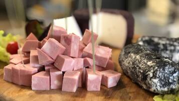 A wooden cutting board with cubed pink ham, a whole cheese, and a sliced black and white cheese.