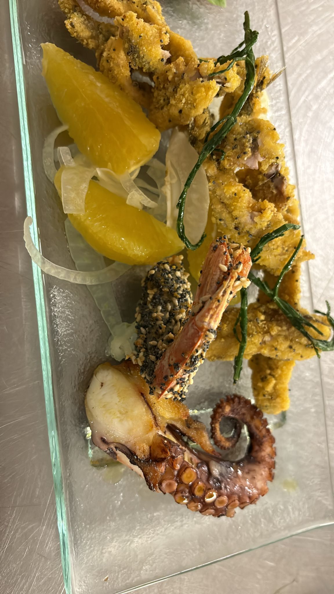 Un plato de mariscos con preparaciones empanizadas y tentáculos de calamar sobre un plato de vidrio.