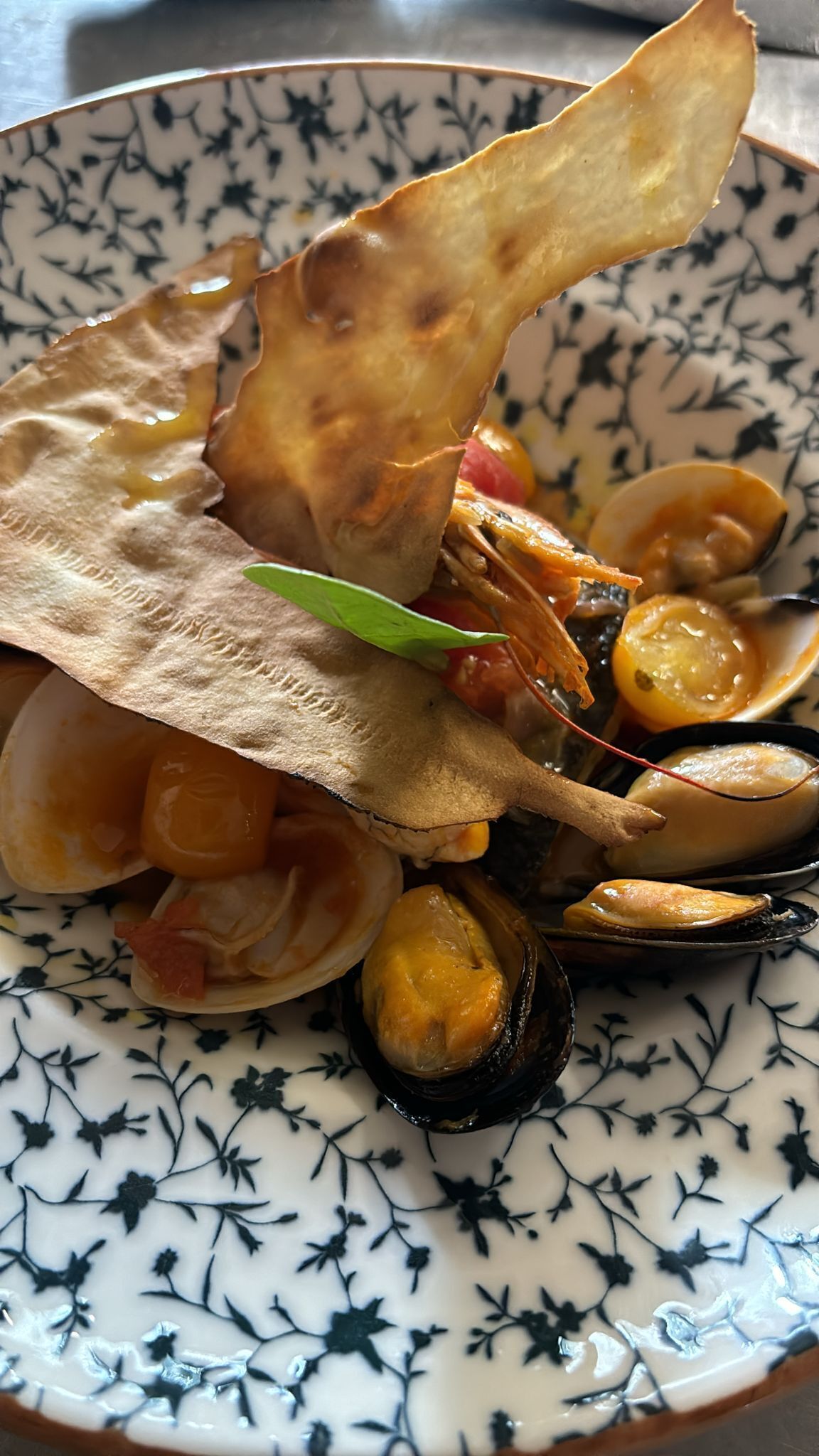 A plate of seafood with mussels and shrimp, served on a patterned ceramic plate.