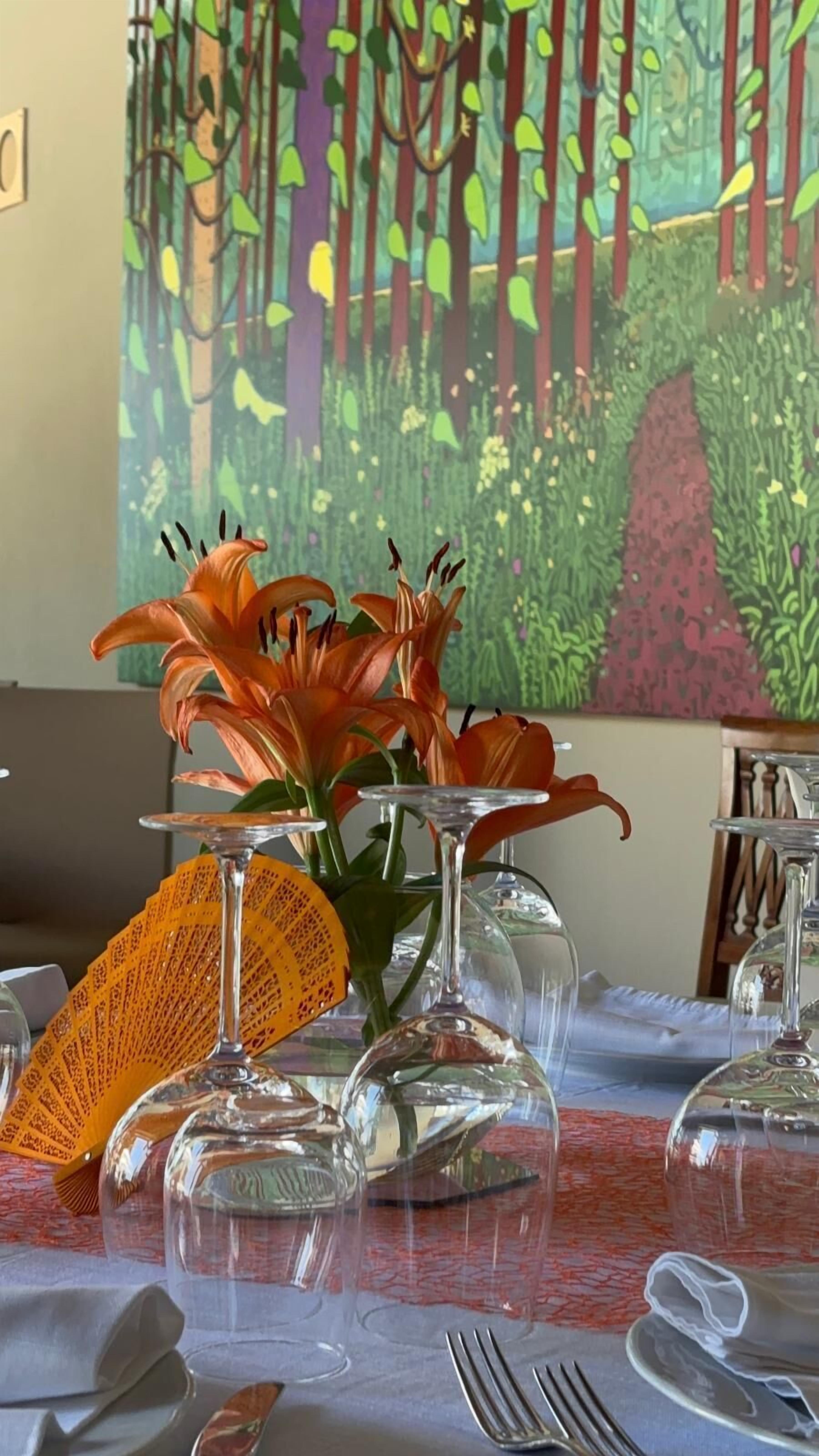 Una mesa de comedor con cristalería transparente, un tejido de punto y un mural con motivos forestales al fondo.