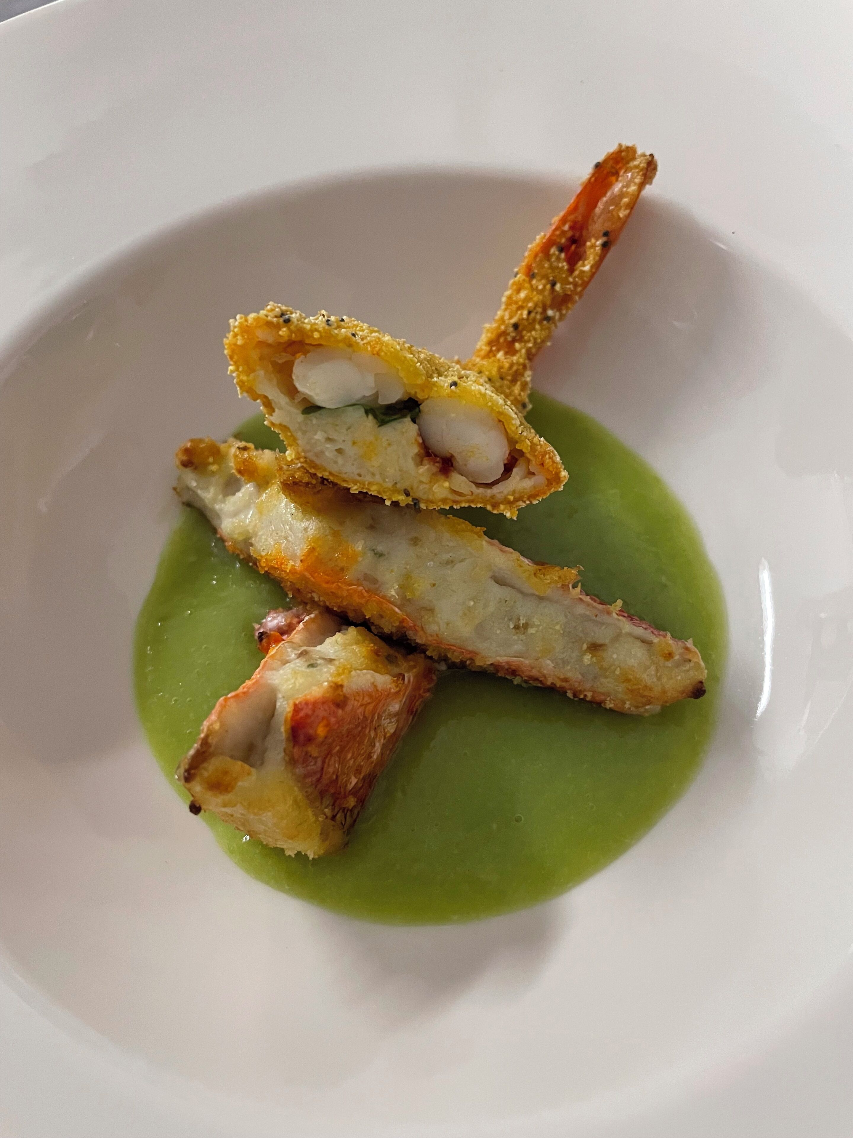 Un plato con un trozo de comida empanizada, posiblemente pollo, y salsa verde.