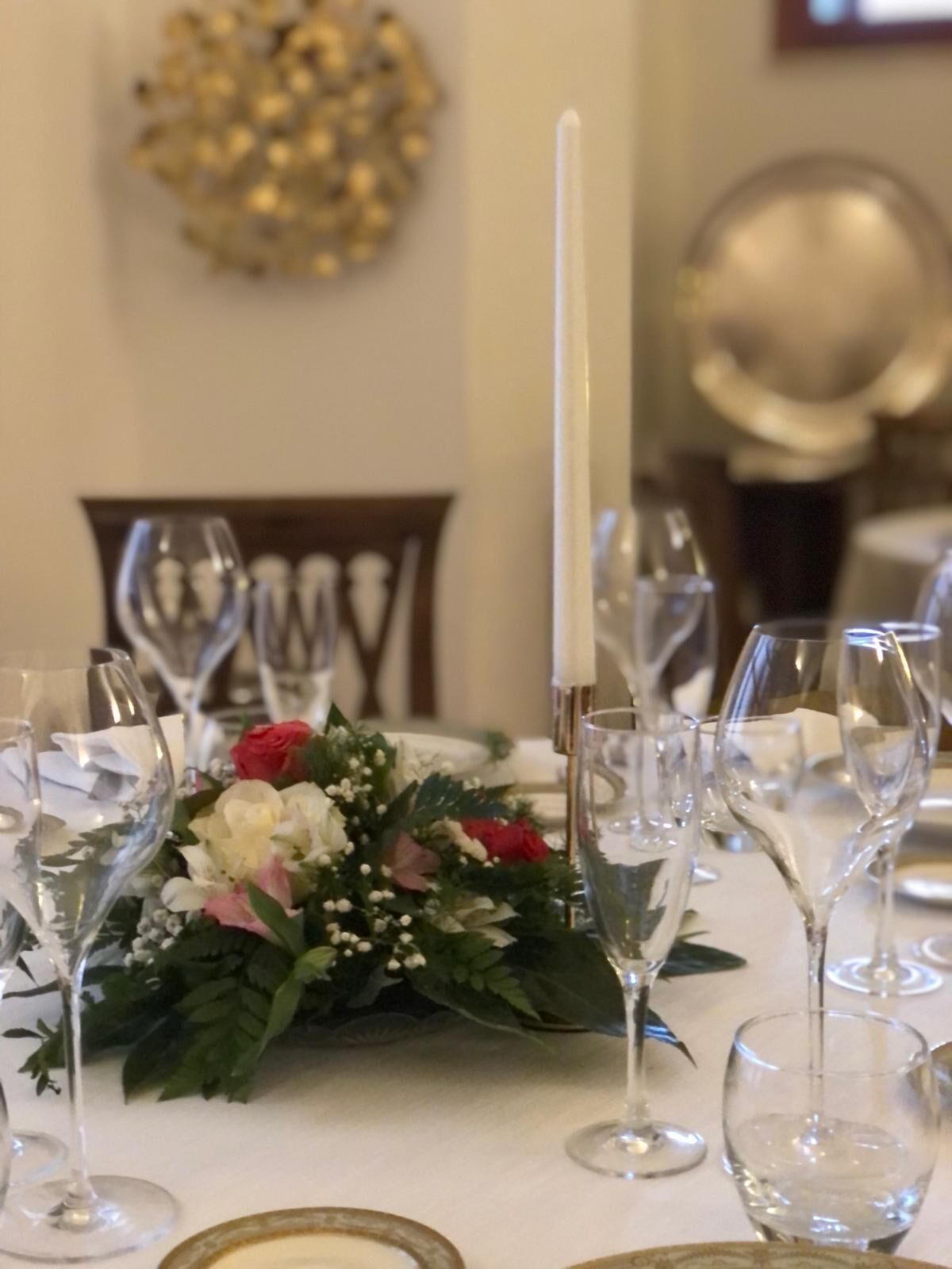 A dining table set with wine glasses, a centerpiece of flowers, and a tall white candle.
