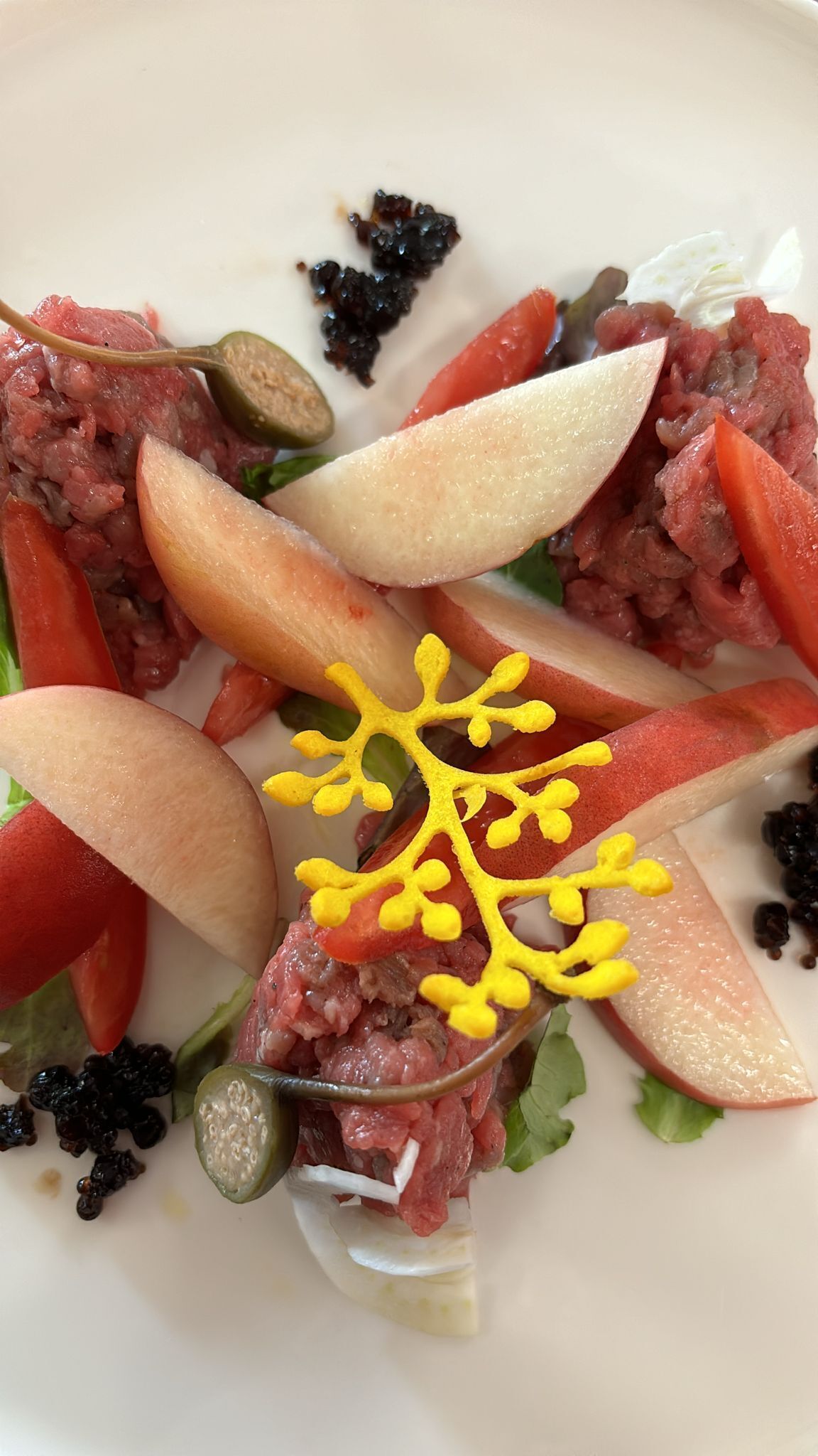 Une assiette contenant un plat à base de viande, des légumes et un élément décoratif jaune.