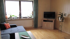 Una sala de estar con un sofá, un televisor sobre un mueble bajo y una planta en maceta.