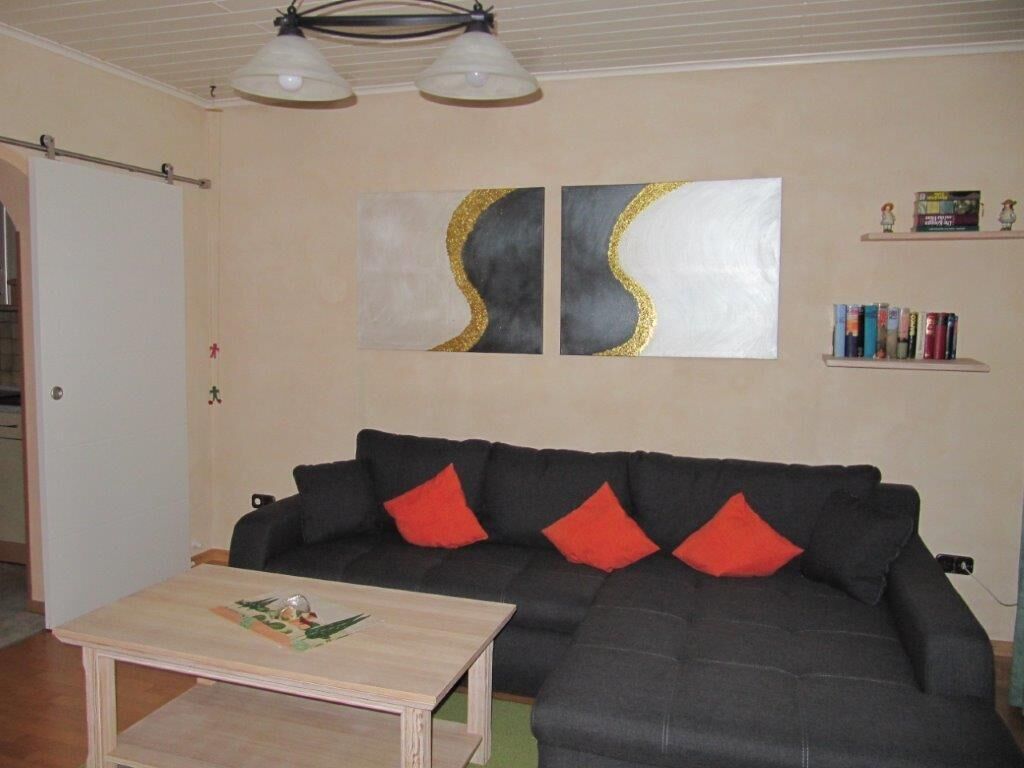 A living room with a dark grey sectional sofa, two red cushions, a wooden coffee table, and two abstract paintings on the wall.