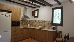 A kitchen with wooden cabinets, a built-in microwave, and a window with a view of trees. - Rural house with garden, barbecue and swimming pool. Sea, mountains, culture, hiking! (Càlig)