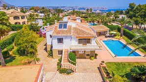 Une maison à deux étages avec une piscine, entourée de palmiers et offrant une vue dégagée sur la mer.