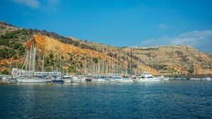 Un port de plaisance où sont amarrés des bateaux, entouré de collines et sous un ciel dégagé.