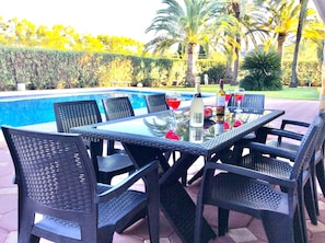Un espace extérieur aménagé pour les repas, avec une piscine, des meubles en rotin noir et une table en verre.