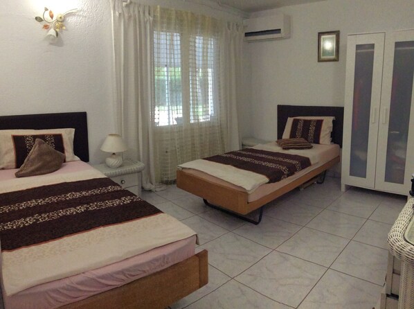A hotel room with two beds, a window with curtains, an air conditioning unit, and a door with a mirror. - Charming villa in Adsubia, with a 40x20-foot pool, air conditioning, and Wi-Fi, a 4-minute drive from the sandy beach (Xàbia)