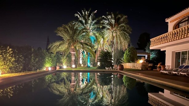 Une vue nocturne d’une piscine bordée de palmiers et d’un bâtiment doté d’un balcon.