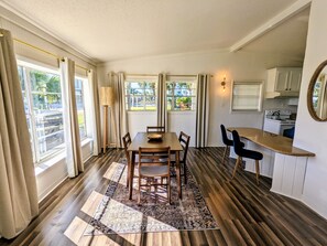 Un comedor con una mesa y sillas de madera, un tapete estampado y vistas al exterior a través de ventanas amplias.