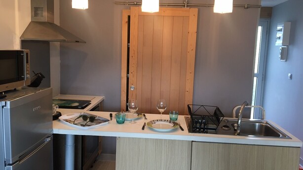 Een moderne keuken met een centraal eiland, roestvrijstalen apparatuur, hangende lampen en een houten deur.