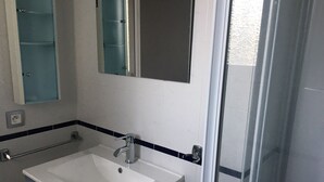 Een badkamer met een witte wastafel, een spiegel en een douchehoek.