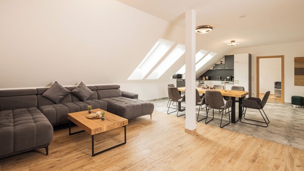 A modern loft apartment with a dining area, a sofa, and a kitchen in the background. - Fantastic luxury apartment in Salzburg's ski paradise (Mauterndorf)