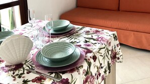 A dining area with a table set for two, featuring floral tablecloth, green plates, and white bowls.