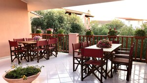 A terrace with a wooden table and chairs, surrounded by potted plants and a railing.