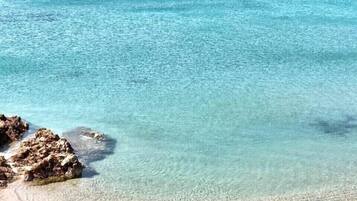 Eine Küstenansicht mit klarem türkisblauem Wasser, einem Boot, Felsen und einem Betonsteg.
