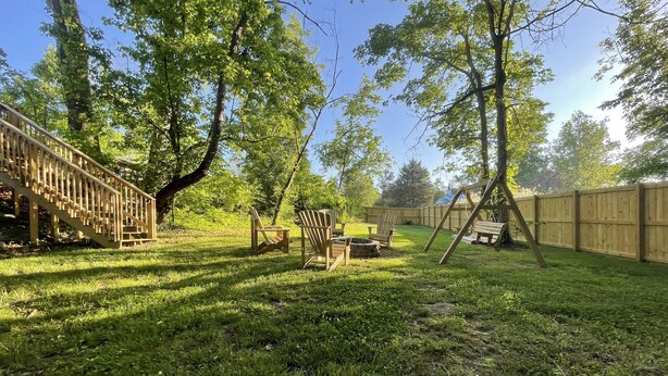 A backyard with a wooden deck, a swing set, and a fire pit area.