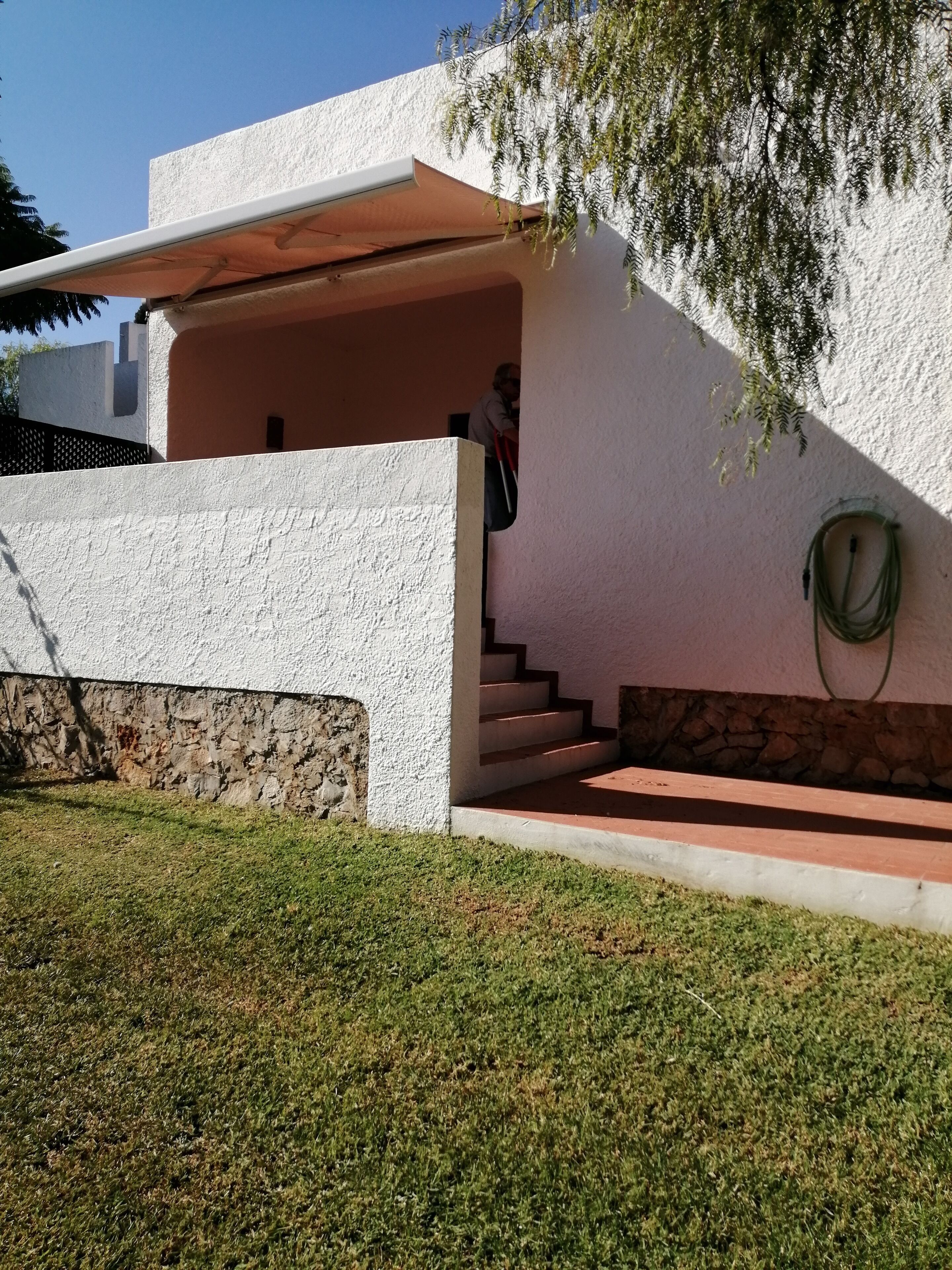 Una casa moderna con fachada blanca, base de piedra y una escalera que conduce a un porche cubierto.