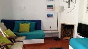 Un soggiorno con un divano blu, cuscini verdi e gialli, sedie in legno, un tavolino da caffè nero, una televisione e un camino con legna.