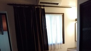 Una camera d'albergo con un letto, una sedia, una finestra con tende e un termosifone.