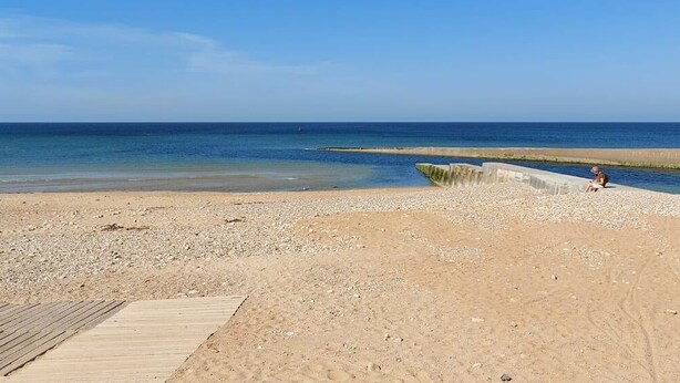 A beach with a wooden boardwalk leading to a concrete structure by the water.