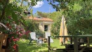 A garden with a patio area, including a table and chairs, and a small building with a tiled roof.