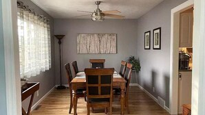 A dining area with a wooden table and chairs, a ceiling fan, and a painting on the wall.