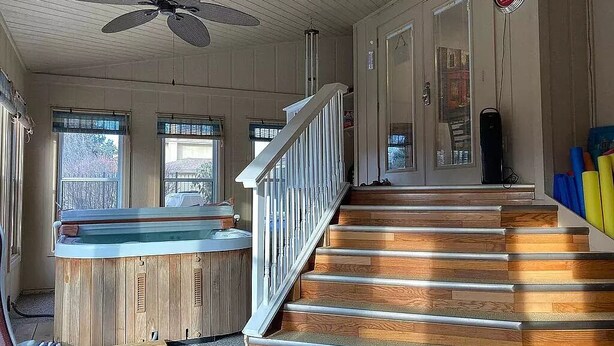 A wooden staircase leading to a second floor, a hot tub, and a ceiling fan.