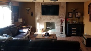 A living room with a fireplace, leather sofa, coffee table, and a television mounted on the wall.
