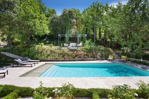 Ein Pool mit einer Pergola und Liegestühlen, umgeben von üppiger Vegetation.