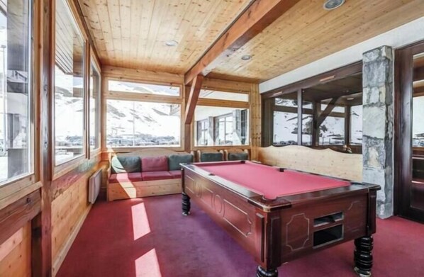 A pool table in a room with wooden walls and large windows.