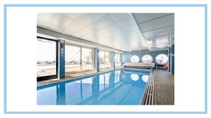 Ein Hallenbad mit großen Fenstern, gefliestem Boden und einer Sitzbank am Rand.