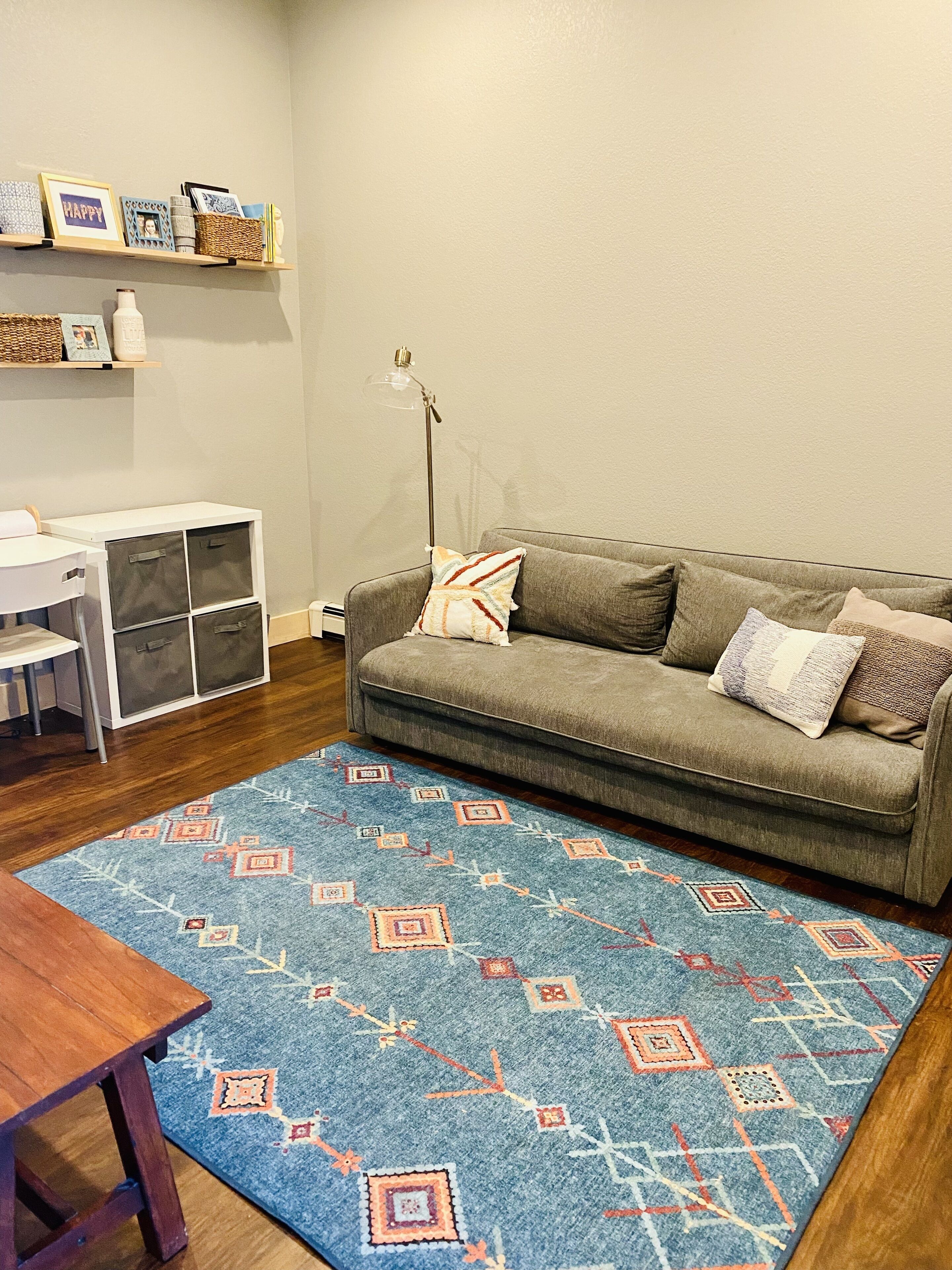 Un salon comprenant un canapé, une table basse, un tapis, un bureau et des meubles de rangement.