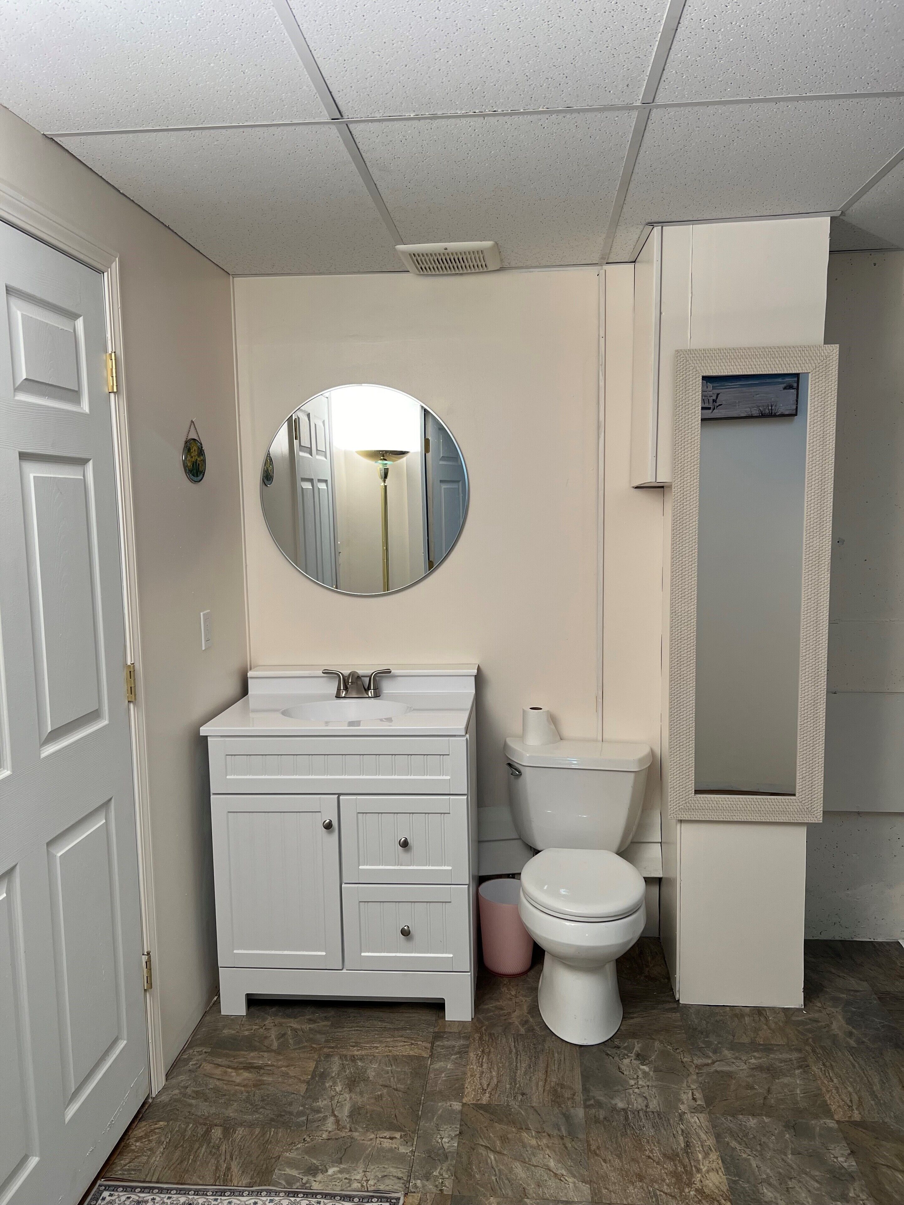 A bathroom with a white vanity, a round mirror, a toilet, and a shower enclosure.