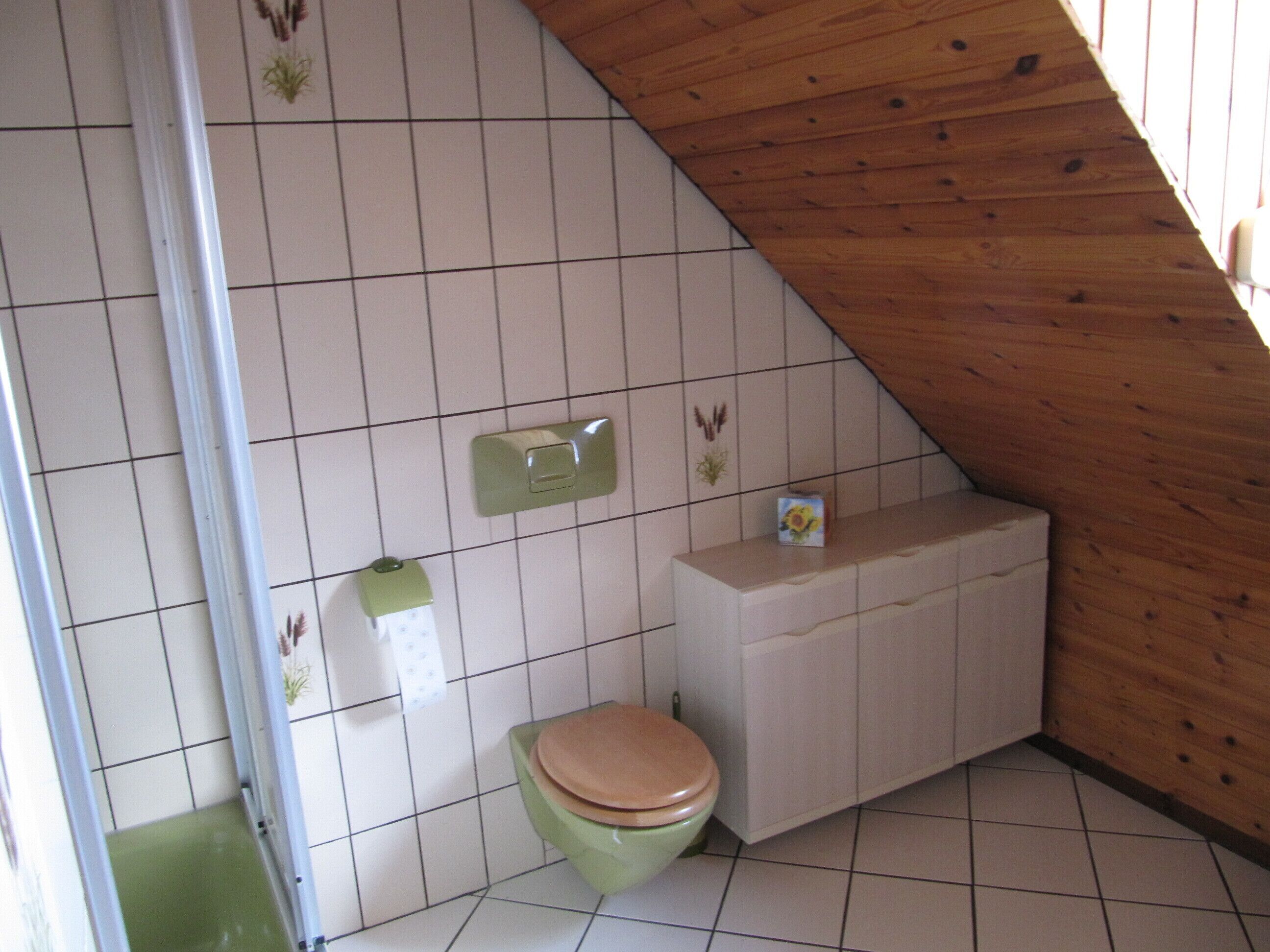 Et lille badeværelse med flisegulv og træloft, et grønt toilet, en hvid vask og et lille skab.