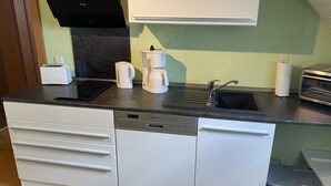 Una cocina compacta con encimera negra, armarios blancos, cafetera, tostadora y lavabo.
