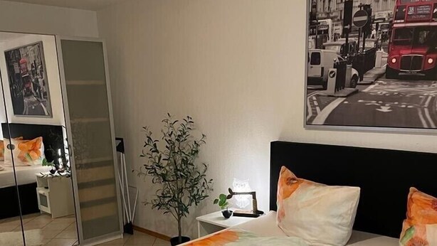A hotel room with a large bed, a nightstand, a mirror, and a painting of a red bus on the wall. - Holiday apartment at Ohrensbächle (Glottertal)