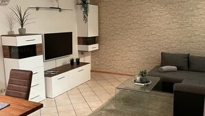A modern living room with a flat-screen TV, white cabinets, a brown leather chair, a glass coffee table, and a grey sofa. - Holiday apartment at Ohrensbächle (Glottertal)